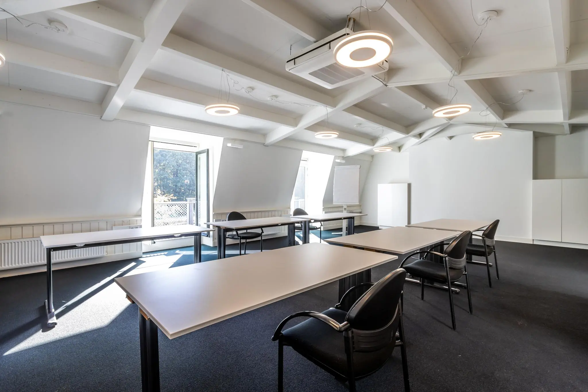 Vergaderruimte aan de Langbroekerdijk A met moderne verlichting, opgestelde tafels en stoelen, en uitzicht op buiten.